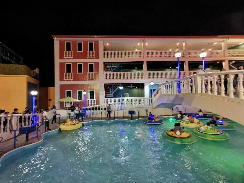 Colorful bumper boats in a turquoise pool under a white bridge at Anjo World at night.