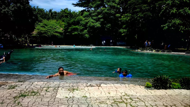 People swimming in a large turquoise lagoon pool surrounded by dense tropical forest.