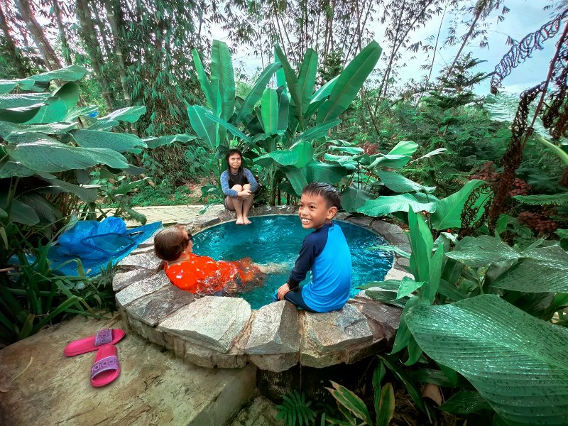 Family relaxing in a small stone-lined turquoise plunge pool surrounded by tropical foliage.