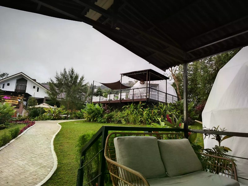 White glamping dome on an elevated deck above stone paths and gardens with misty mountains.