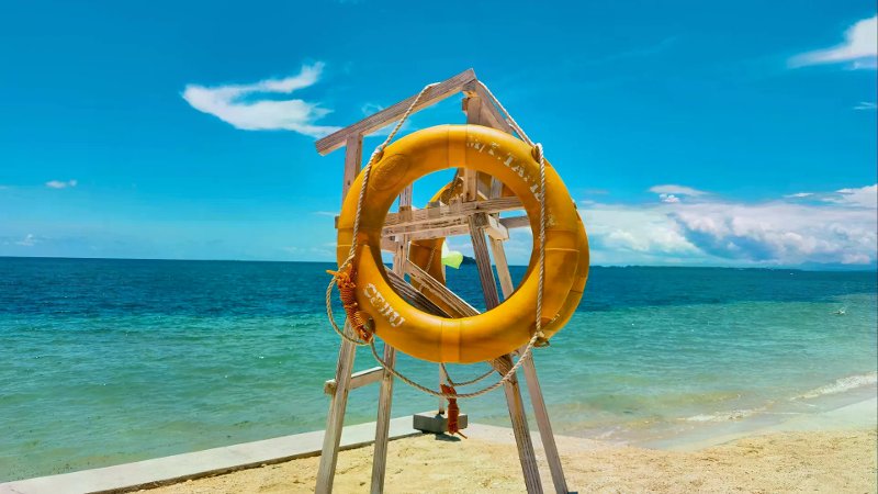 Bright yellow lifebuoy on a wooden stand overlooking turquoise sea and sandy beach.