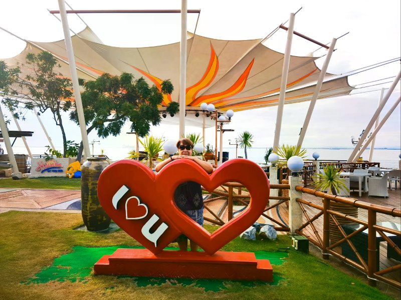 Guest behind a red I love you heart sign near Havana By The Sea deck and ocean view.