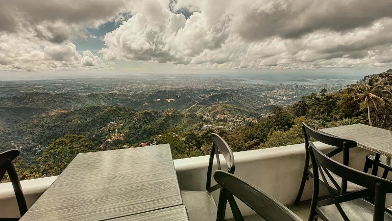 Outdoor terrace tables overlooking lush mountains and the Cebu City skyline under cloudy skies.