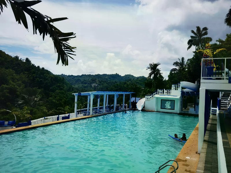 Blue-and-white Santorini-style pool with water slide overlooking lush green mountain ridges.