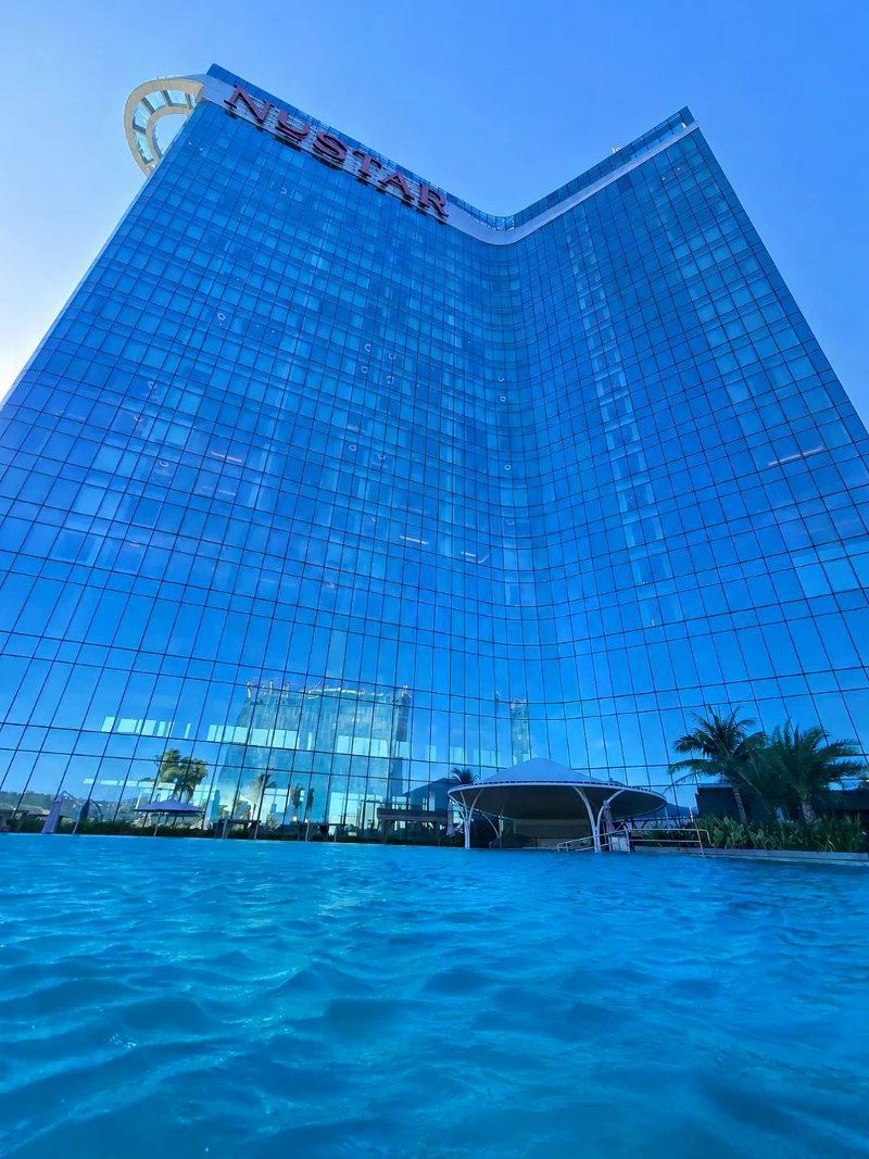 Blue glass Nustar tower with red rooftop letters rising above a rippling infinity pool.