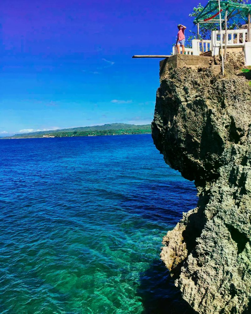 A massive coral rock cliff with a diving platform overlooking the deep blue sea and coastline at Buho Rock Resort