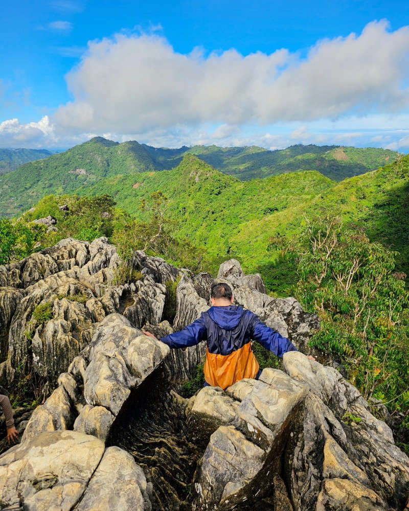 緑の山々の尾根を見渡す絶景を背景に、マヌンガル山の険しい石灰岩の岩場を進むハイカー。