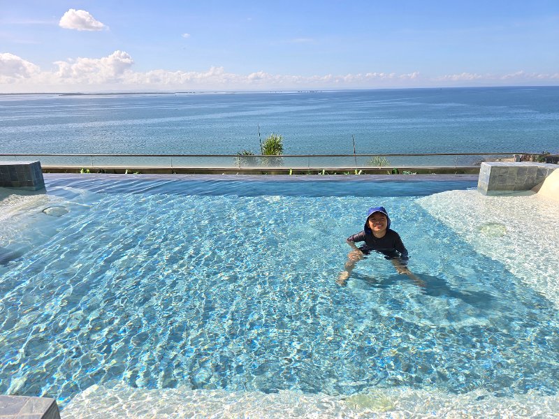 A child wearing a sun hat and rash guard enjoying the oceanview infinity pool at NUSTAR Resort Cebu overlooking the Mactan Channel.