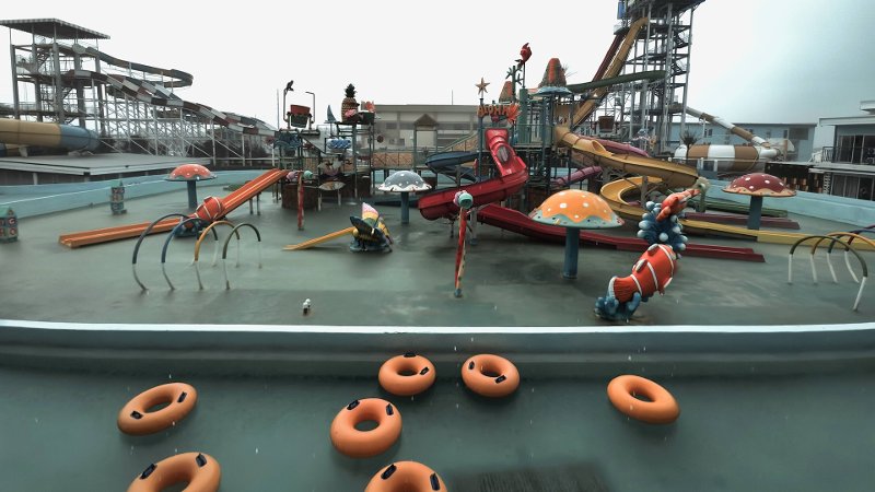 A children's water play area at WaterWorld Cebu featuring multiple colorful water slides, aquatic structures, mushroom sprinklers, and orange inflatable inner tubes floating in the shallow pool foreground under an overcast sky.