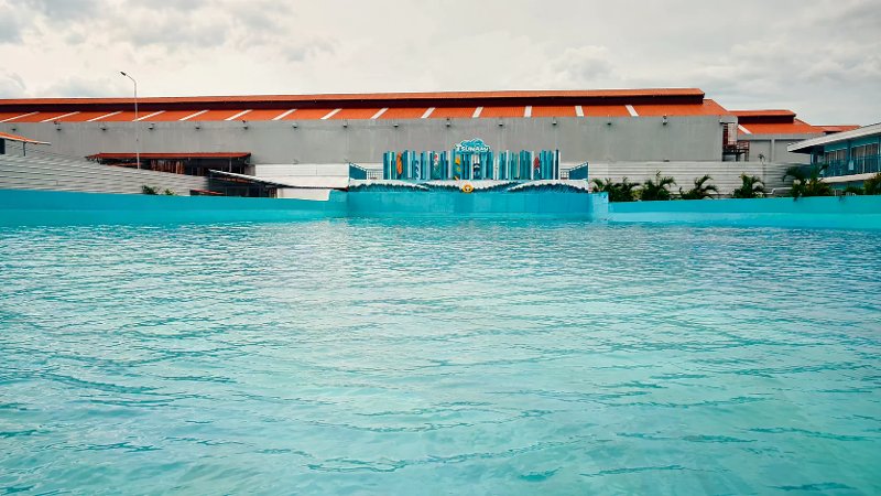 Clear turquoise water in a wave pool at WaterWorld Cebu, set against a wave-generating wall with a orange-roofed building visible in the background.