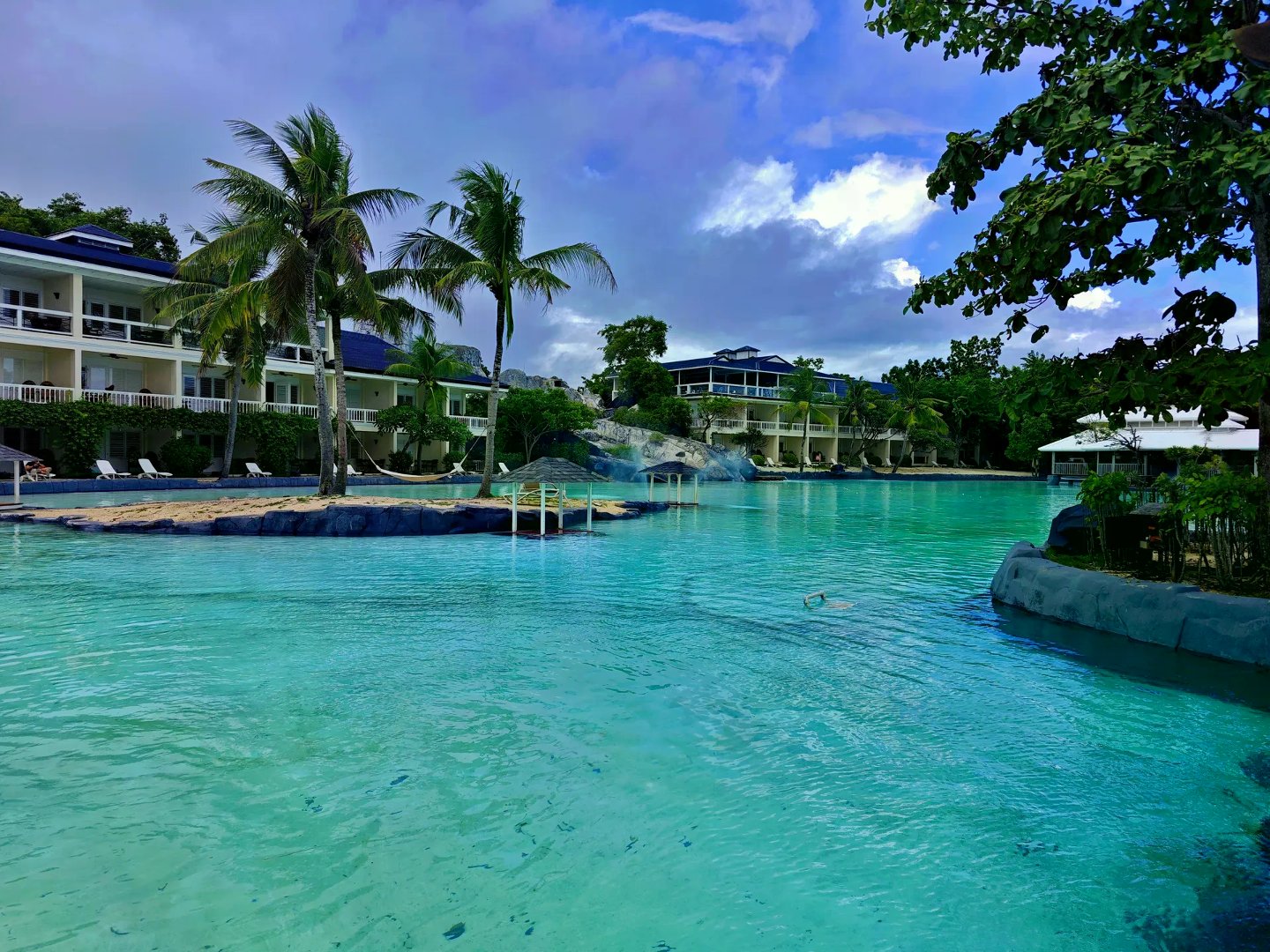 Expansive turquoise saltwater lagoon with palm island and multi-story resort rooms along the shore.