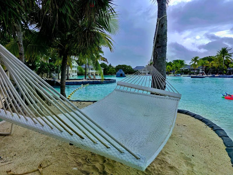 White woven hammock between palms overlooking a large turquoise lagoon under dramatic clouds.