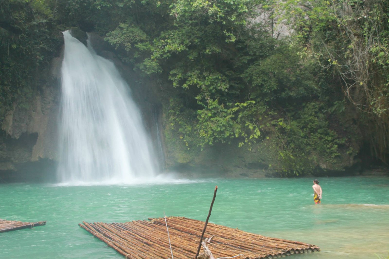 Traditional bamboo raft floating in the vivid turquoise basin of Kawasan Falls