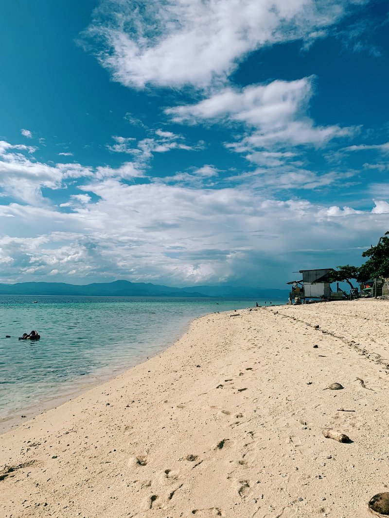 Wide white sand shoreline and clear blue sea at Basdako Beach in Moalboal.