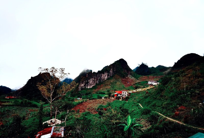 Panoramic view of lush green mountain peaks and terraced hills in Badian under an overcast sky, with scattered buildings nestled in the landscape.