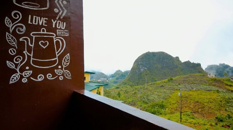 View from Patimz Bistro balcony showing a brown wall with white coffee artwork alongside a scenic view of rolling green hills.