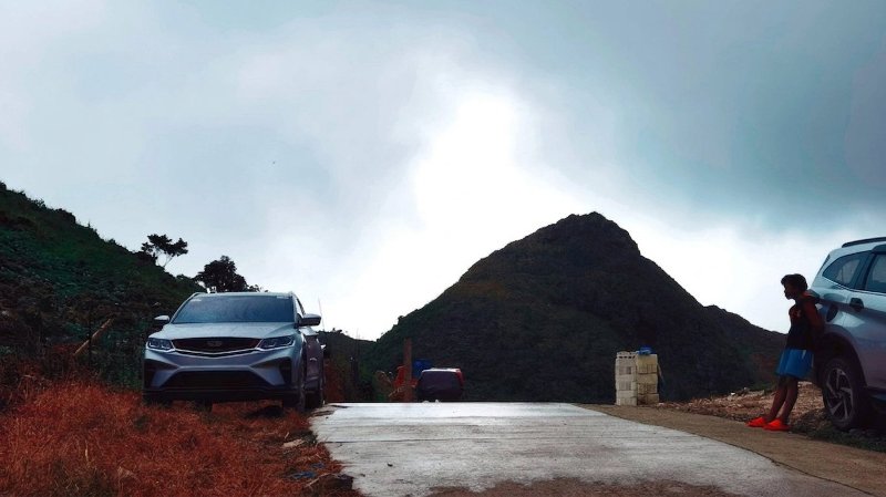 A gray SUV parked along a wet mountain road in Badian with dark, pointed green peaks framing the misty background.