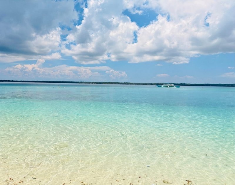Clear, shallow turquoise ocean waters stretching toward the horizon under a cloudy blue sky in Bantayan, Cebu.