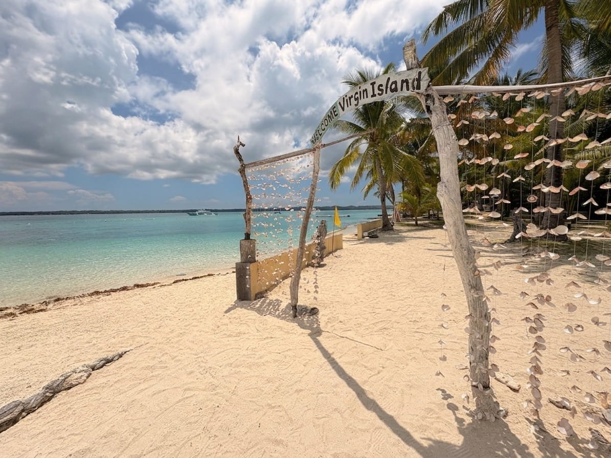 A rustic wooden archway decorated with dangling seashells on a sandy beach looking toward clear turquoise water.